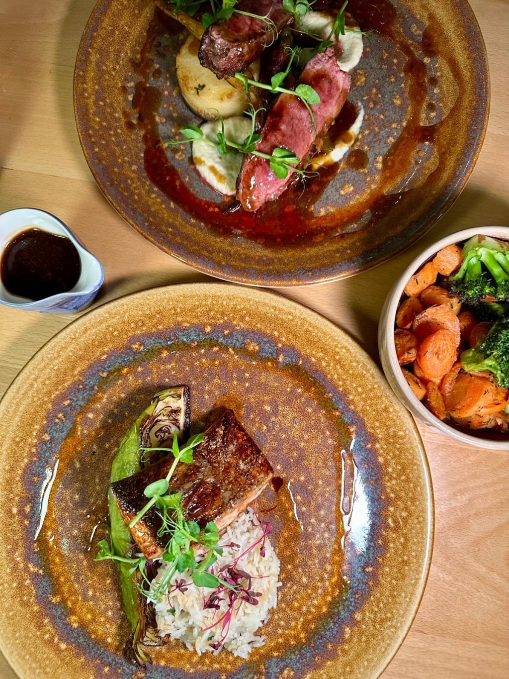 A gourmet plate featuring honey and soy glazed salmon alongside seared duck breast, accompanied by fondant potatoes, pickled blackberries, and miso-roasted Hispi cabbage.