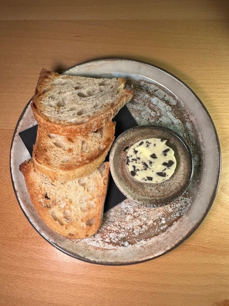 A plate of freshly baked bread with a golden crust, served with a side of smooth, creamy olive butter.