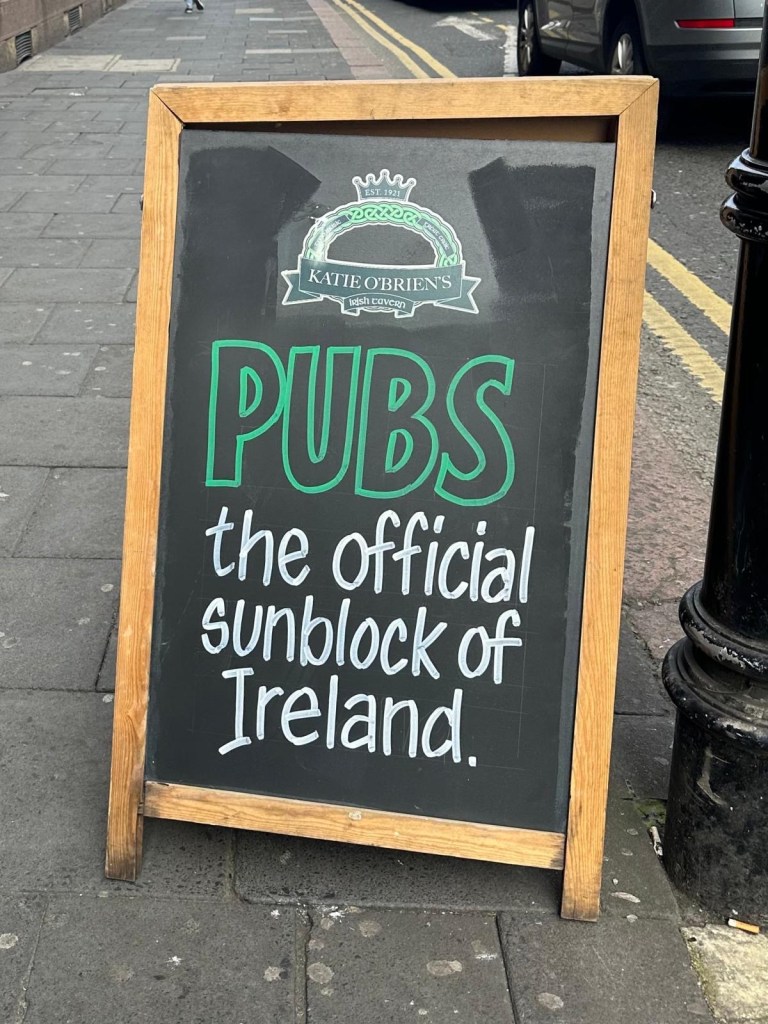 A sandwich board outside Katie O’Brien’s Irish bar in Newcastle, featuring a witty and humorous message welcoming guests.