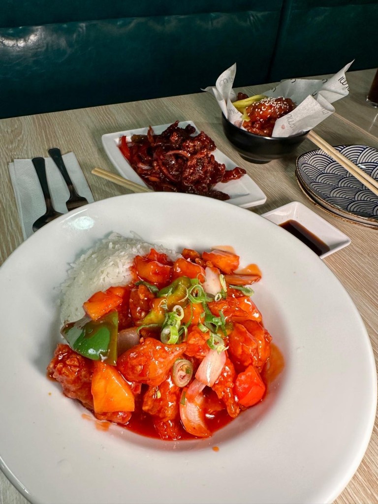 A vibrant sweet and sour chicken dish, with golden-fried chicken pieces coated in a glossy, tangy sauce.
