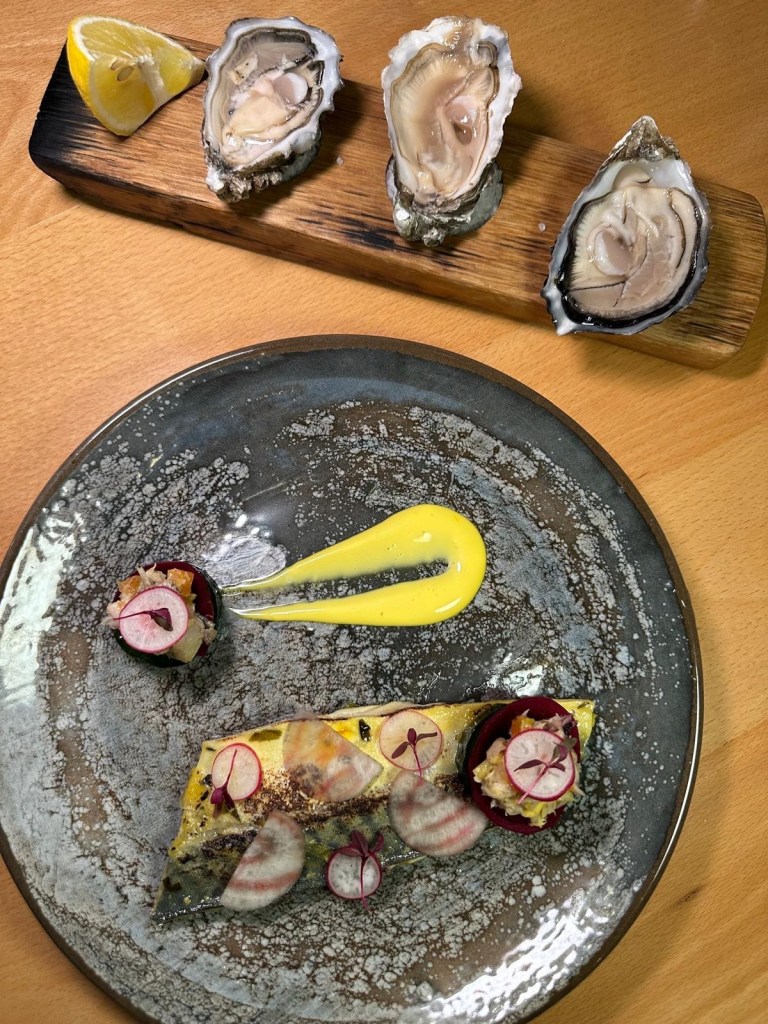 A seafood platter featuring fresh Lindisfarne oysters on the half shell alongside mackerel escabeche, served with saffron mayonnaise, sourdough bread, and compressed cucumber.