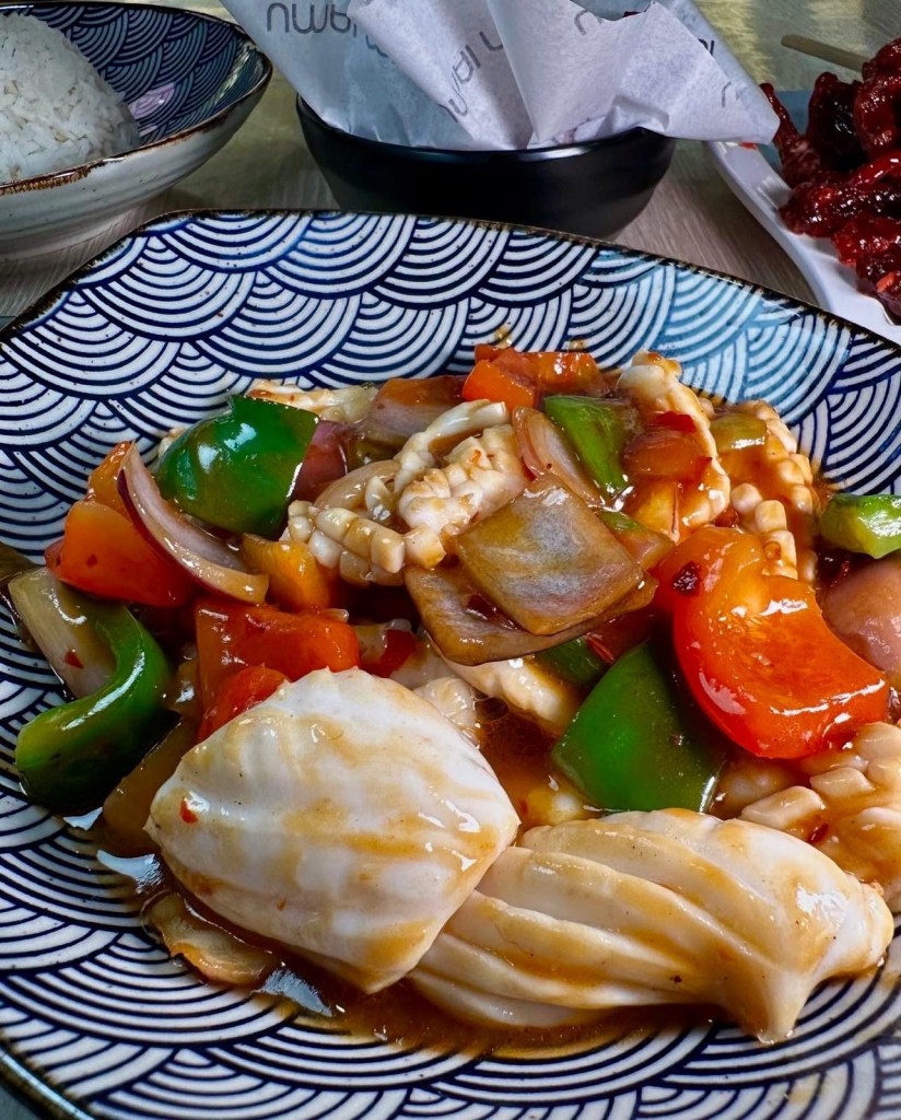 A generous portion of stir-fry squid rolls, served with fresh vegetables and garnished with aromatic herbs.