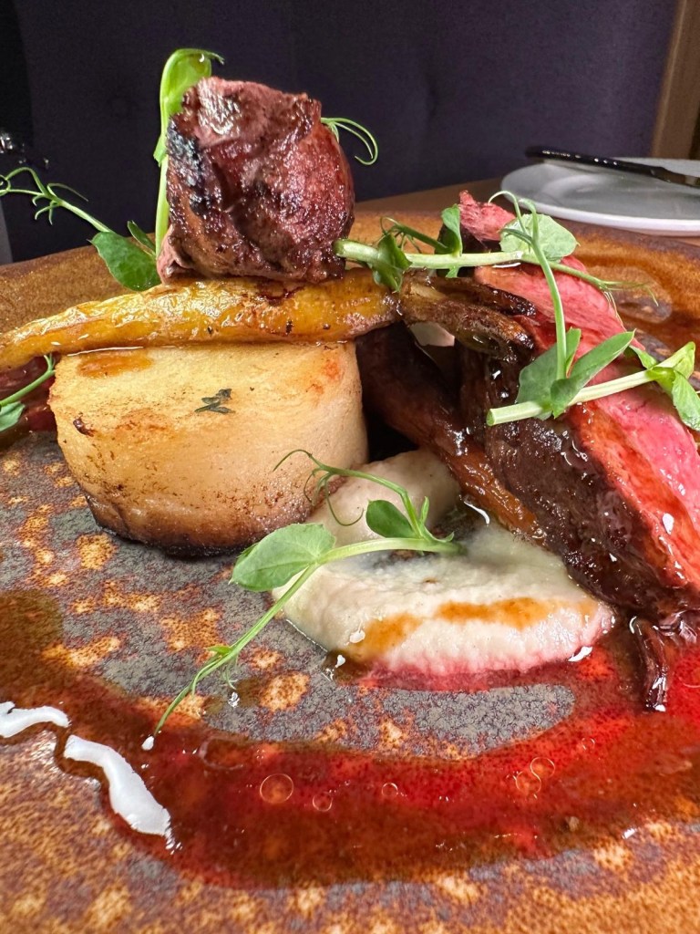 A gourmet dish featuring seared duck breast with golden fondant potatoes, pickled blackberries, and celeriac-apple purée.