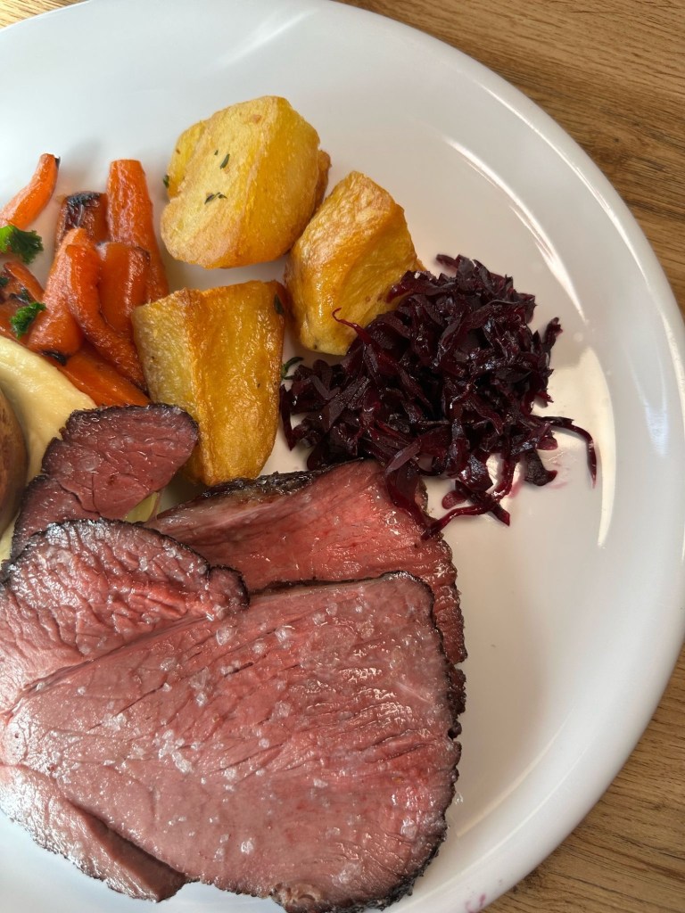 A perfectly plated roast beef dinner with tender slices of beef, crispy roast potatoes, vibrant vegetables, and a rich Yorkshire pudding.