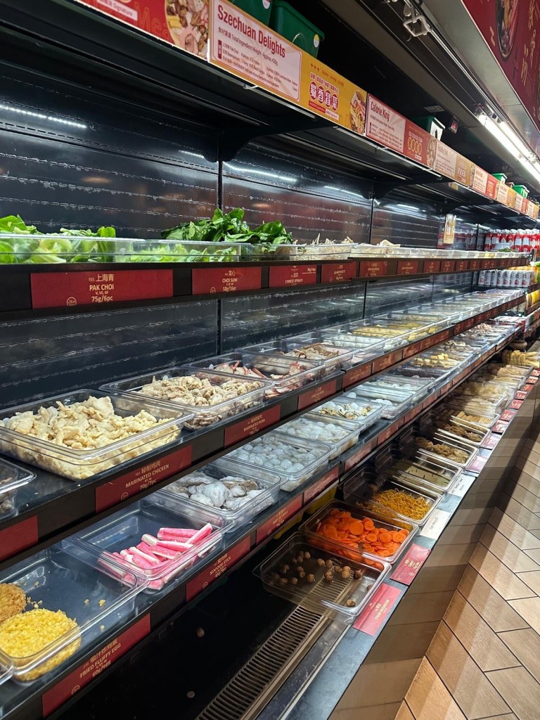 A well-stocked selection fridge at Malatang Express, filled with fresh vegetables, meats, seafood, and noodles for a custom Malatang bowl.