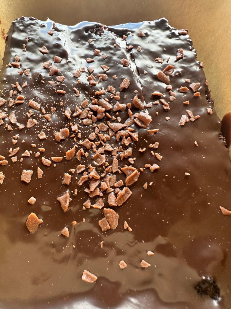 A rich and moist slice of Matilda chocolate cake from Spud Life Newcastle, dusted with cocoa and served on a white plate.