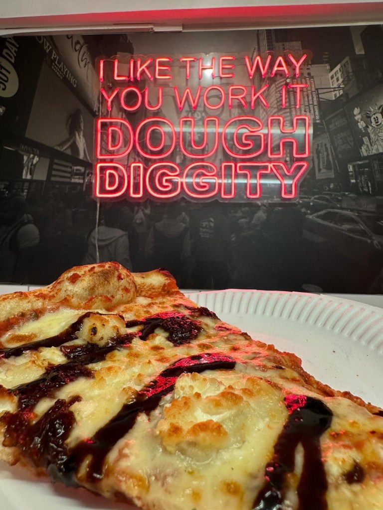 A large New York-style pizza topped with creamy goat’s cheese, tangy red onion jam, and a balsamic drizzle on a golden, thin crust.