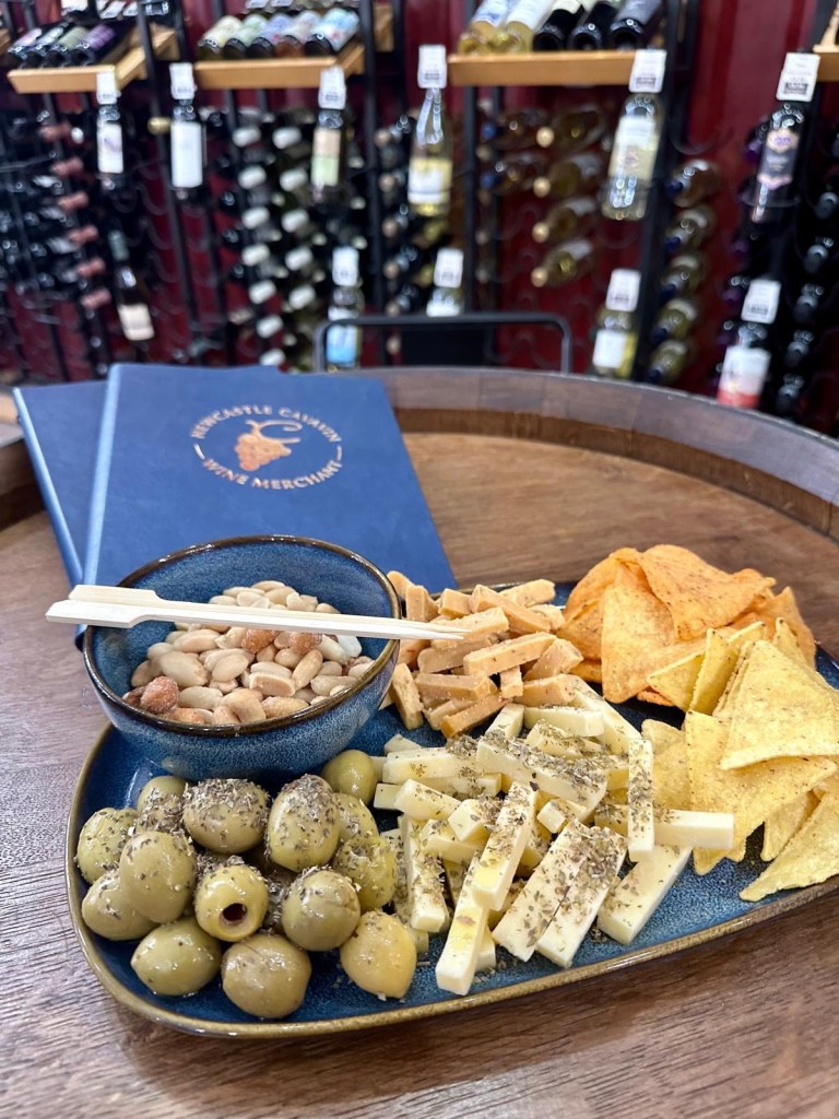 A delicious snack platter at Newcastle Cavavin featuring olives, cheese, nuts, and crisps, served alongside glasses of wine.