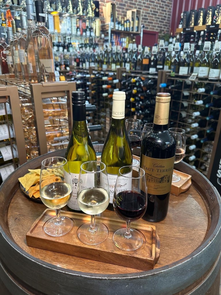 A beautifully arranged wine flight at Newcastle Cavavin, featuring three elegant glasses of red, white, and rosé wine on a wooden tray.