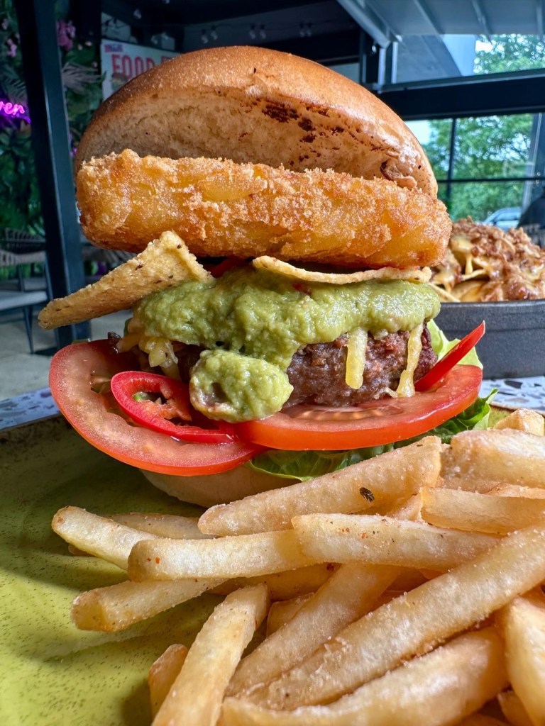 Vegan Green Mexican burger stacked with guacamole, jalapeños, nachos, and a hash brown