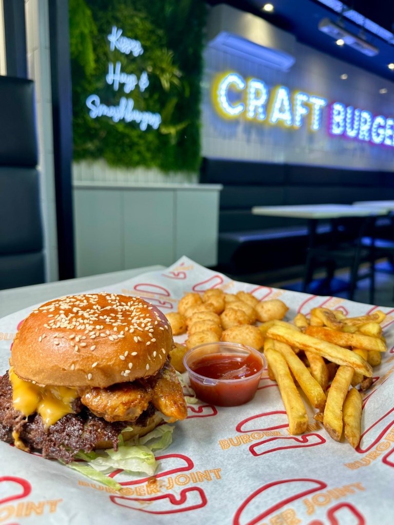 A vibrant table full of Craft Burger favourites at the Gosforth venue — featuring the Cheetos Smash Burger, New Yorker Boss Box, loaded chilli fries, Tayta tots, buffalo hot tenders, and house dips, all set against the fun, modern interior of the new branch.
