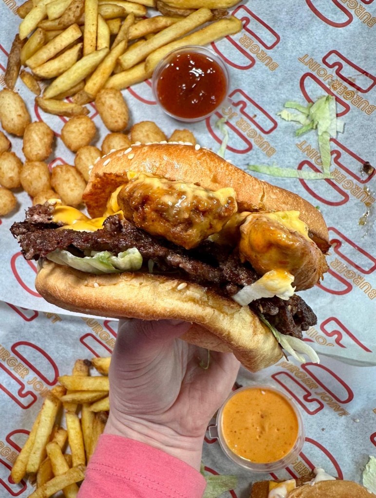A vibrant table full of Craft Burger favourites at the Gosforth venue — featuring the Cheetos Smash Burger, New Yorker Boss Box, loaded chilli fries, Tayta tots, buffalo hot tenders, and house dips, all set against the fun, modern interior of the new branch.