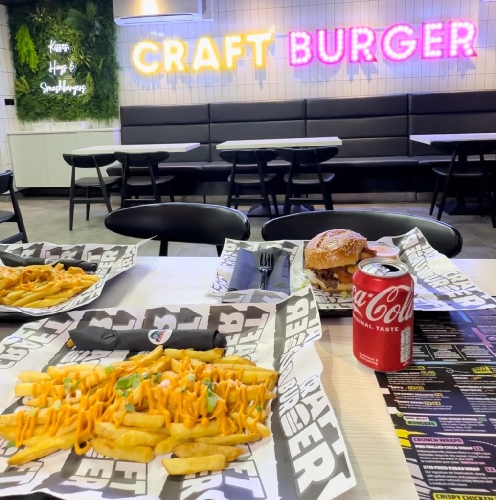 A vibrant table full of Craft Burger favourites at the Gosforth venue — featuring the Cheetos Smash Burger, New Yorker Boss Box, loaded chilli fries, Tayta tots, buffalo hot tenders, and house dips, all set against the fun, modern interior of the new branch.