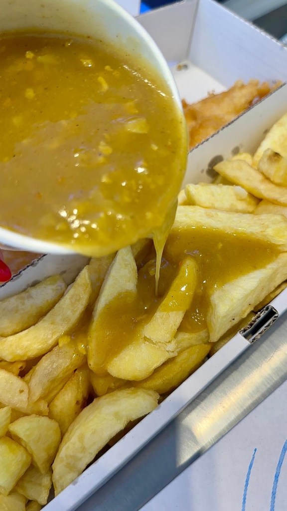 Curry sauce being poured over chips at Krispies Fish & Chips in Forest Hall