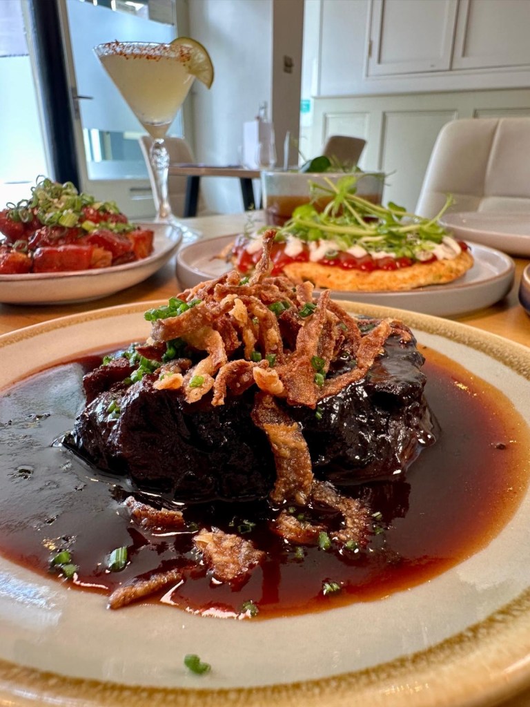 Slow cooked beef topped with black garlic mayo, gherkin ketchup, and crispy onions at Isla in Durham.