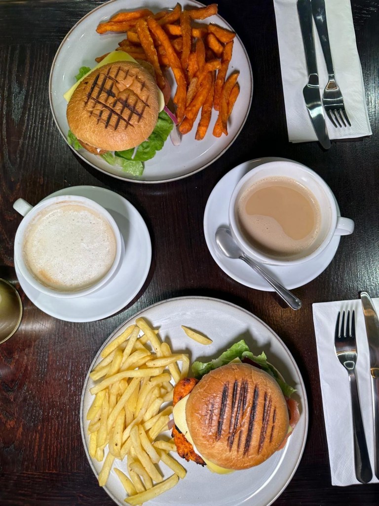 Selection of brunch dishes at Olive Kitchen Newcastle including vegan burger, peri peri chicken burger, fries, cheesecake, and Malteser slice.