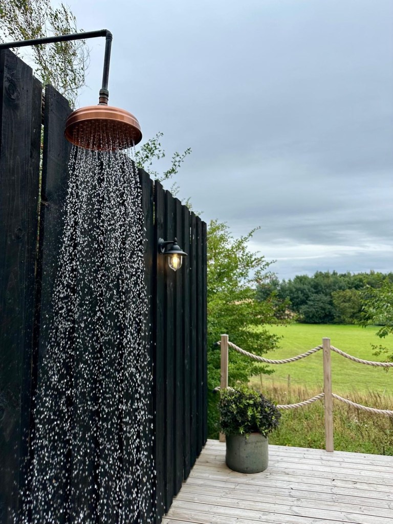 Scandinavian-style outdoor sauna with wooden deck, sun loungers, and a refreshing cold drench shower at Hewn Yorkshire.
