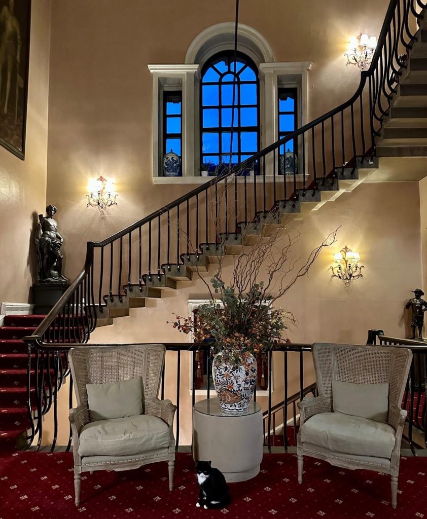 Grand staircase inside Lumley Castle Hotel with chandelier lighting and portraits along the walls.