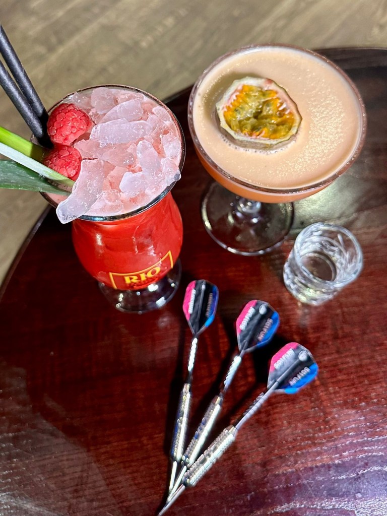 Cocktails placed beside darts at Bullseye Social Darts in Jesmond, showing colourful drinks and the interactive darts setup.