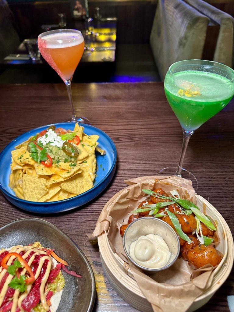 Cocktails and small plates at Manahatta Newcastle, featuring vibrant drinks alongside dishes like frickles, salt and pepper squid, sticky chicken bites and truffle waffle fries.