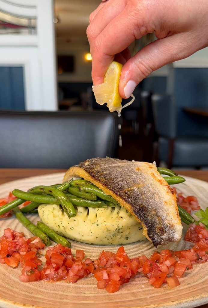 Lemon being squeezed over pan seared seabass with tomato salsa at The Queen's Head Cullercoats