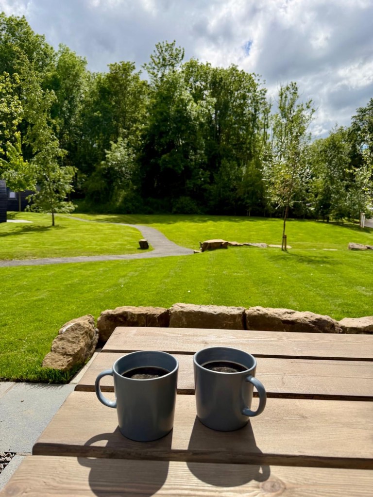 Coffee on the outdoor table outside a Hewn Yorkshire cabin overlooking fields and woodland